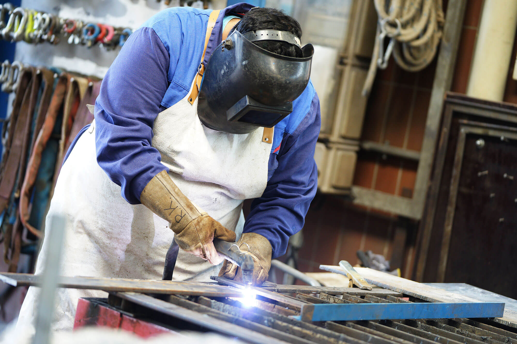 Metalltechniker_reiling Ein engagierter junger Mann in seiner Ausbildung als Metalltechniker. Mit einer schwarzen Schweißer-Maske, einer Schweißer-Schutzschürze und Handschuhen ausgestattet, schweißt er konzentriert ein Stück Metall. Seine Hingabe zum Handwerk zeigt sich in jeder Schweißnaht.