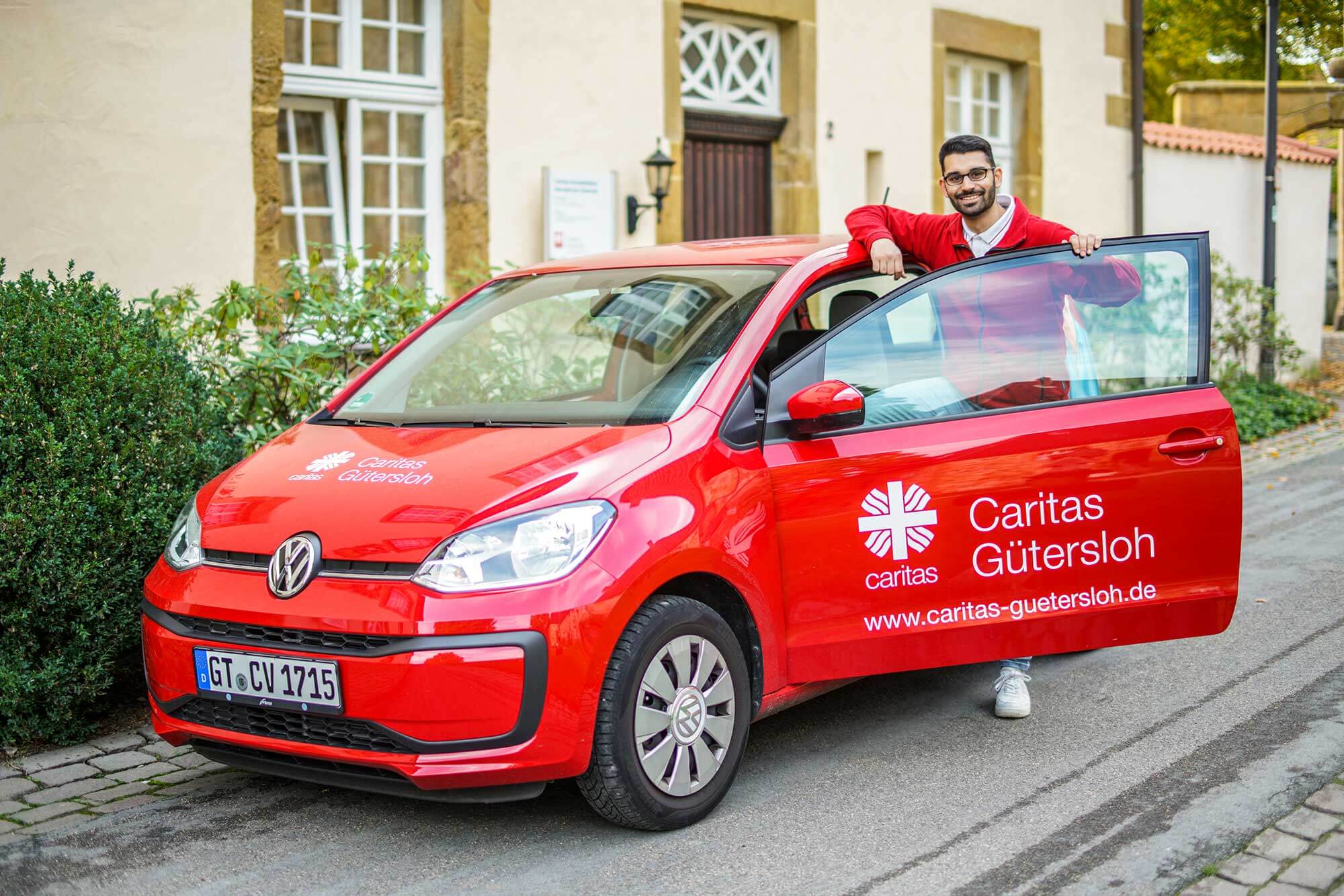 Mit Freude unterwegs: Unser Caritas-Mitarbeiter auf dem Weg zum nächsten Hausbesuch Ein freudiger Caritas-Mitarbeiter steht vor seinem kompakten Auto, bereit für seinen nächsten Hausbesuch und strahlt die Freude an seiner Arbeit aus