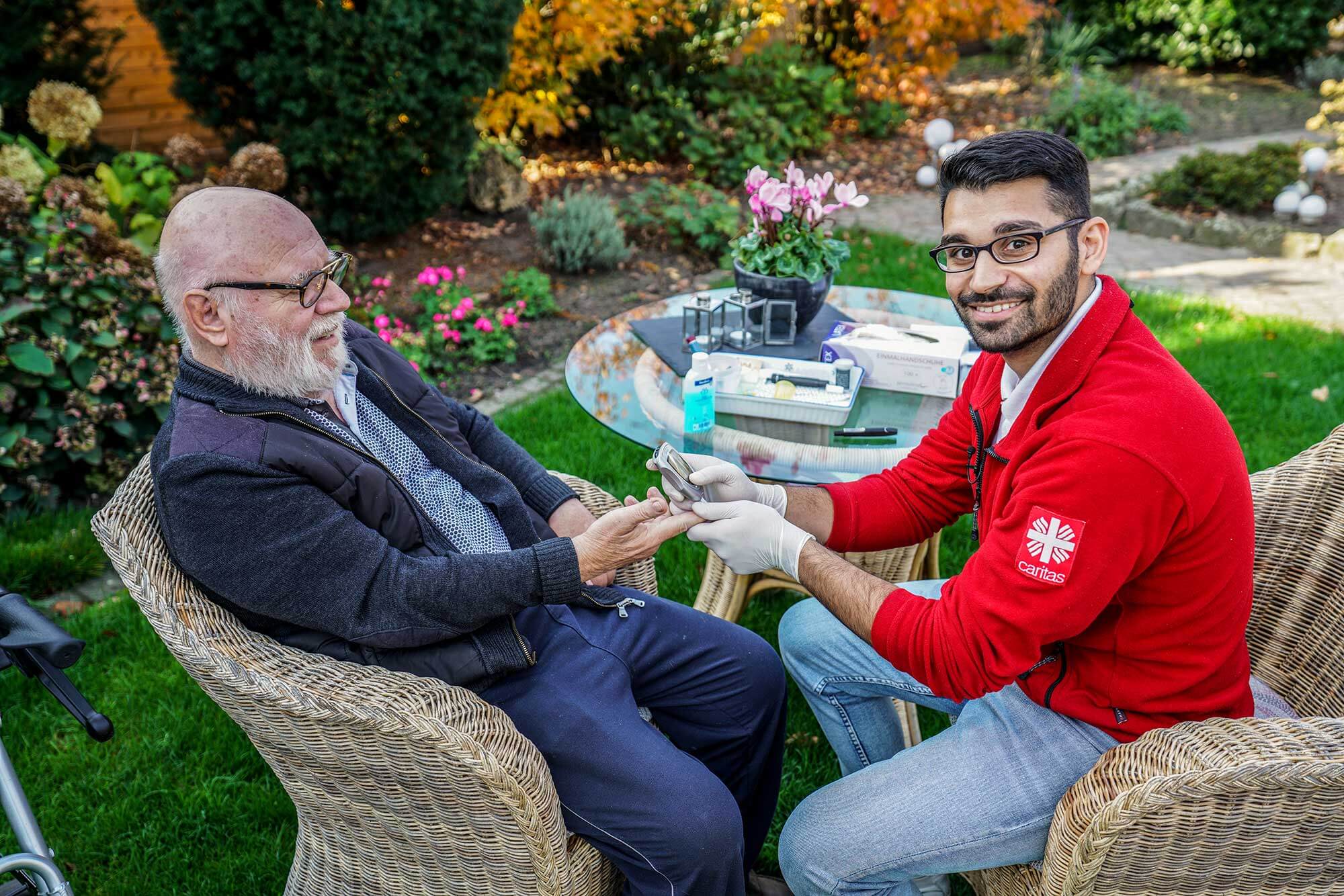 Fürsorge im Alltag: Unsere Caritas-Mitarbeiter in Aktion Ein aufmerksamer Caritas-Mitarbeiter besucht einen älteren Herren zu Hause und misst fürsorglich seinen Blutzuckerspiegel.