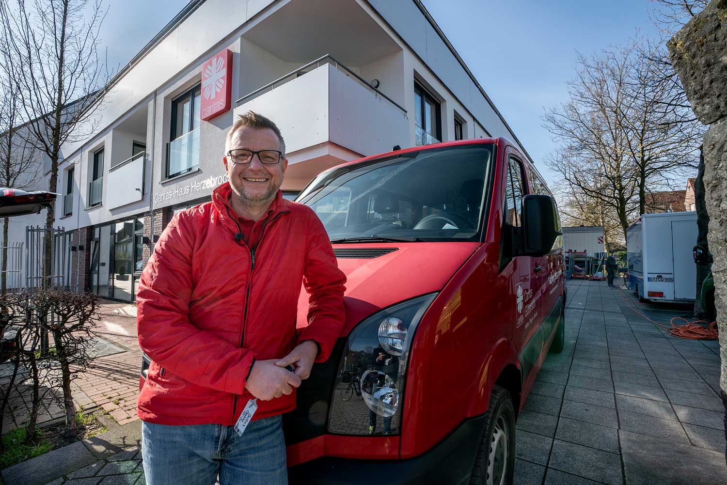 Für unsere Lieblingsmenschen: Unser Caritas-Mitarbeiter auf seiner täglichen Tour Ein Caritas-Mitarbeiter steht stolz vor dem Caritas-Gebäude und seinem treuen Fahrzeug, mit dem er täglich seine 'Lieblingsmenschen' besucht.