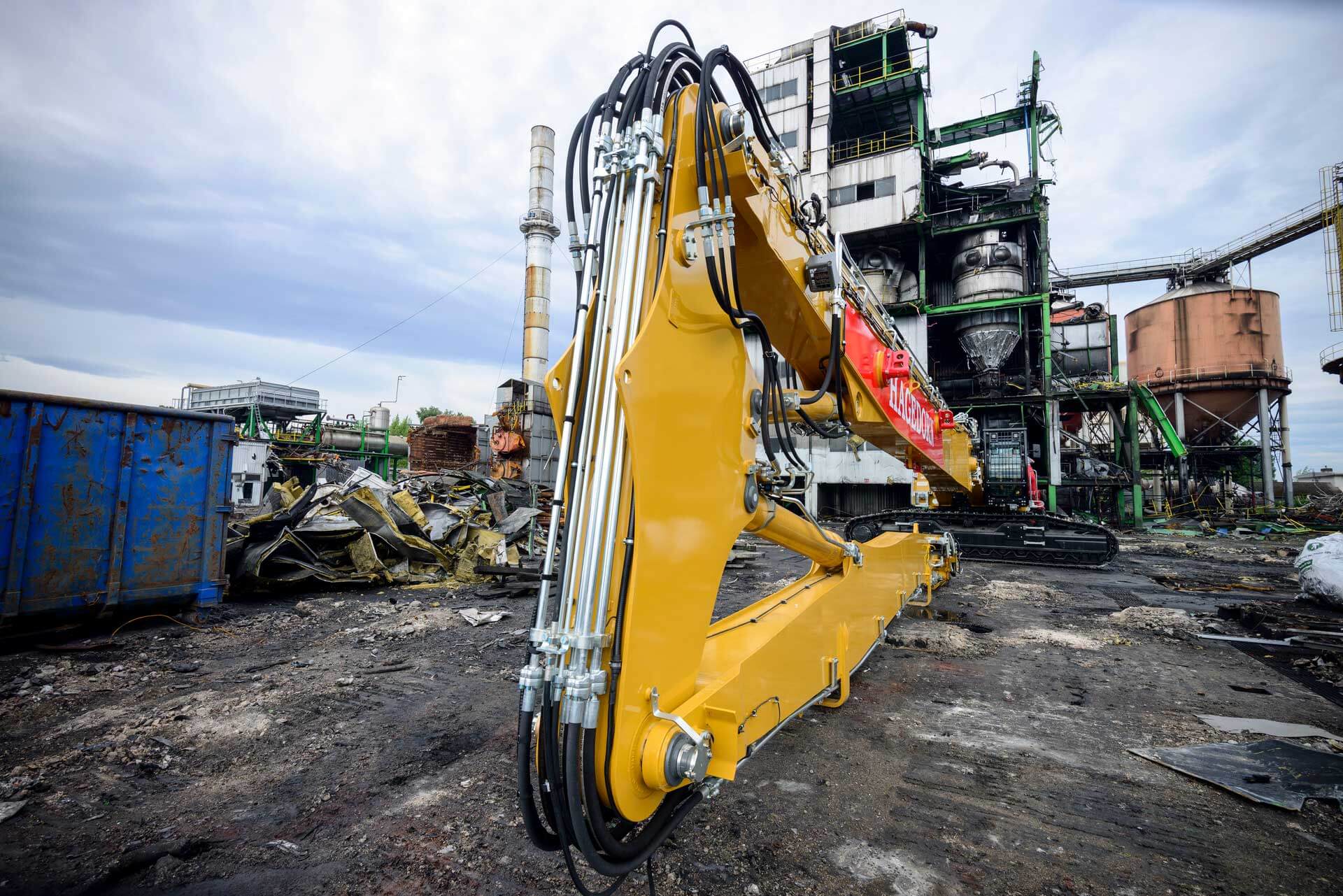 Long-Front Bagger Hagedorn Eine eindrucksvolle Baustellenszene: Der gewaltige LongFrontBagger von Hagedorn steht im Vordergrund, während im Hintergrund eine abgerissene Industrieanlage zu sehen ist. Das Bild vermittelt eine kinoreife Atmosphäre und verdeutlicht die imposante Größe und Kraft dieses beeindruckenden Baggers.