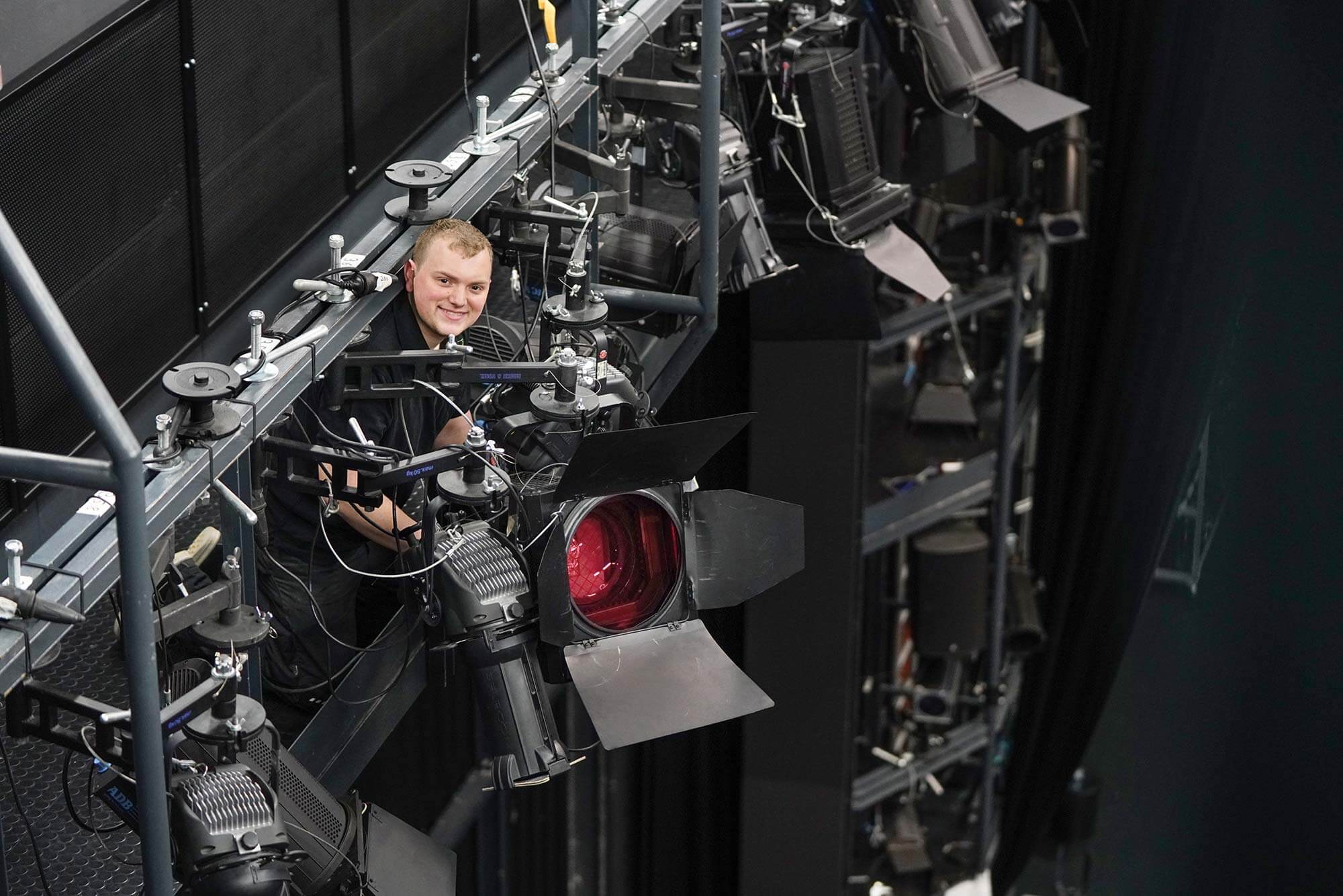 Lichtkünstler im Stadttheater: Unser talentierter Veranstaltungstechniker Ein junger Veranstaltungstechniker richtet das Licht an einem Scheinwerfer im Stadttheater aus, um ein perfektes Bühnenbild zu schaffen.