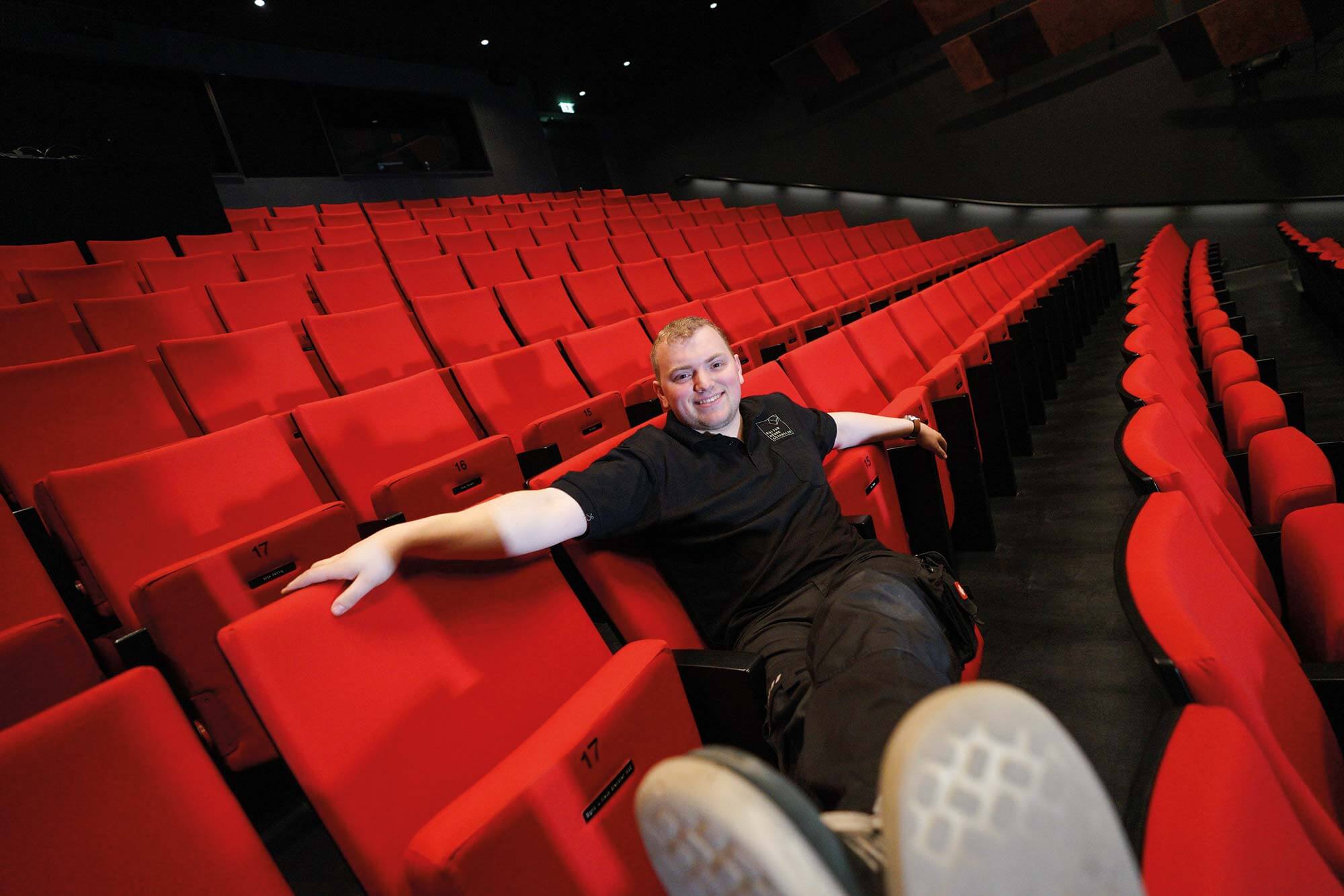 Einladende Atmosphäre: Unser Mitarbeiter im Stadttheater fühlt sich wie zu Hause Ein glücklicher junger Mitarbeiter entspannt im Saal des Stadttheaters und genießt seine Arbeit in diesem inspirierenden Umfeld.