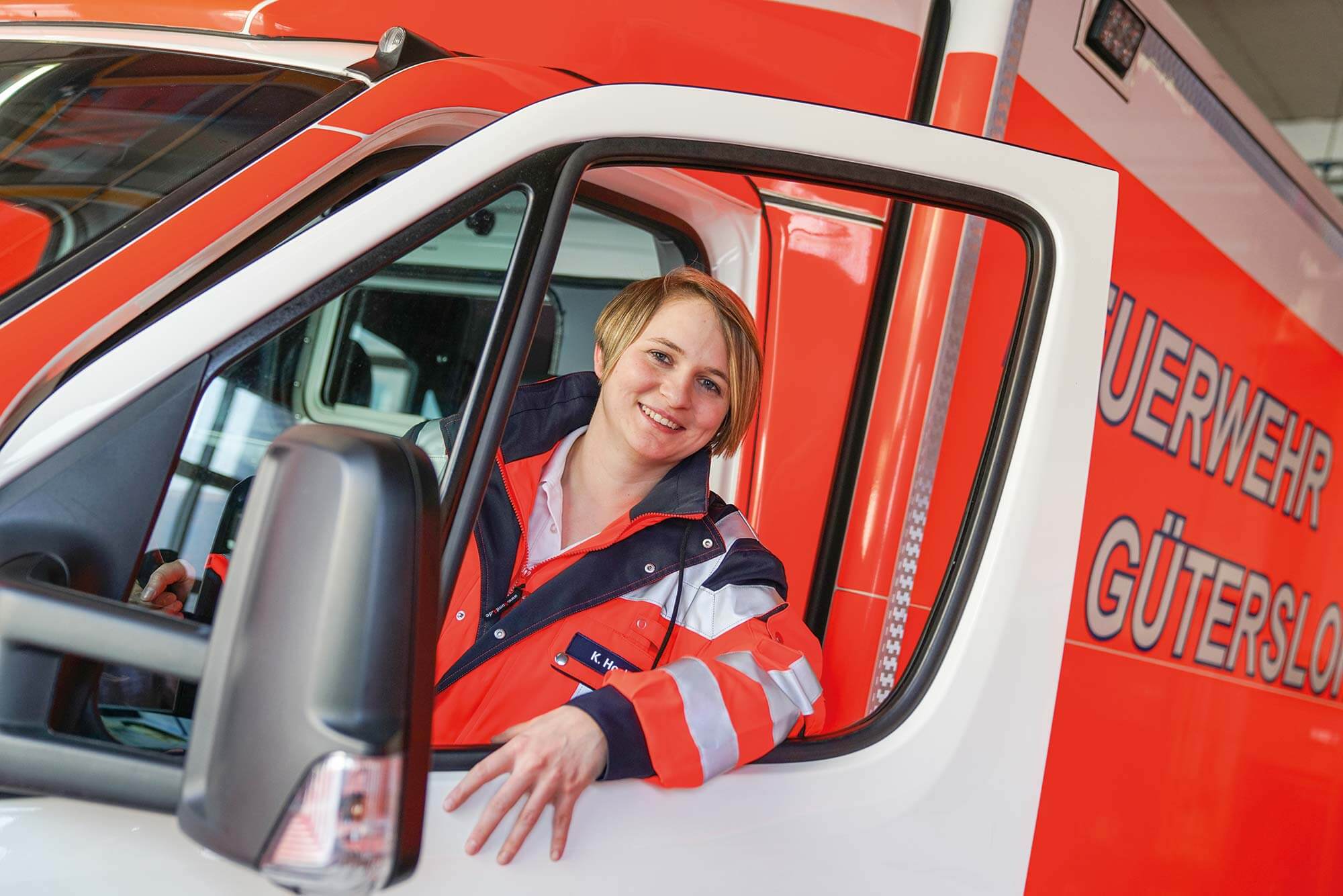 Bereit zum Helfen: Unsere junge Rettungssanitäterin in Gütersloh Eine junge Rettungssanitäterin, die aus dem Rettungswagen schaut und zur Teilnahme an unserem Team in Gütersloh einlädt.